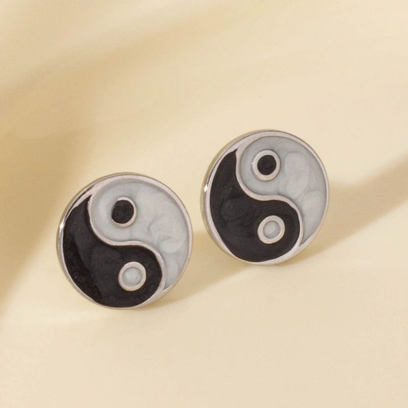 Boucles d'oreilles yin yang en argent posées sur un fond beige lumineux, mettant en valeur leur finition soignée et leur design zen.