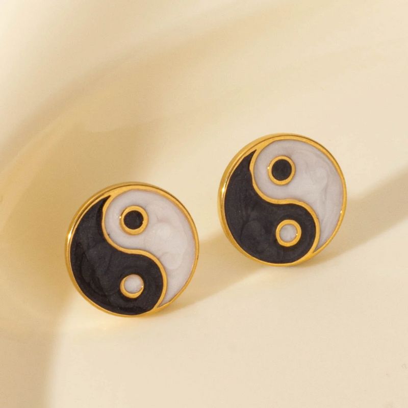 Boucles d'oreilles yin yang en or captant la lumière sur un fond beige, accentuant leur éclat raffiné et leur symbole d'équilibre.