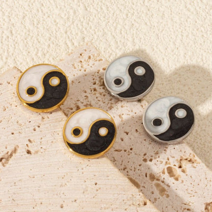 Ensemble de boucles d'oreilles yin yang en or et argent, disposées sur un fond texturé.